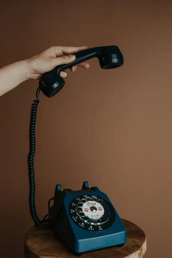 A hand holding the handset of a blue vintage phone