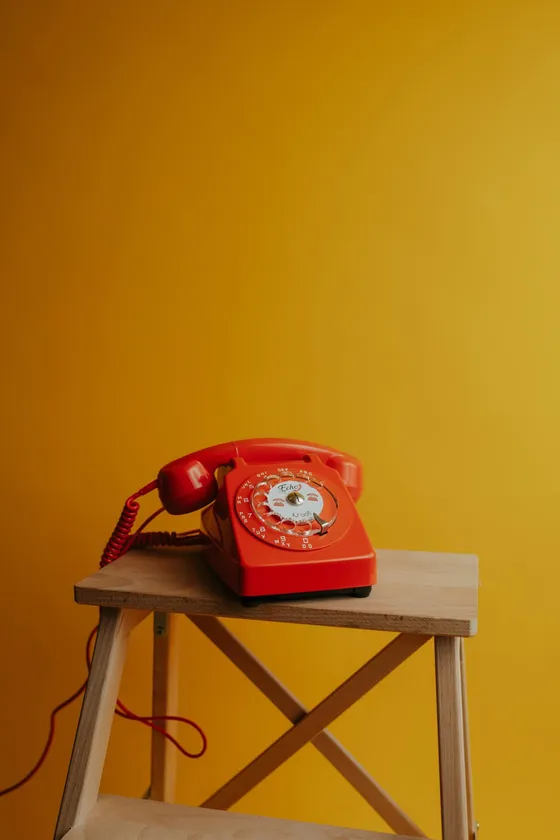 Red phone on a stool against a yellow wall